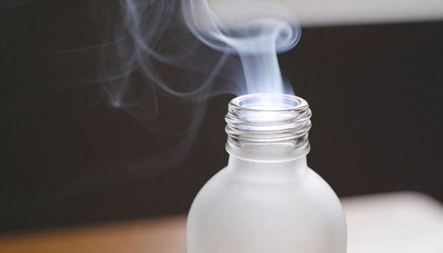 Frosted glass bottle releasing delicate vapor stream on dark backdrop, closeup moody still