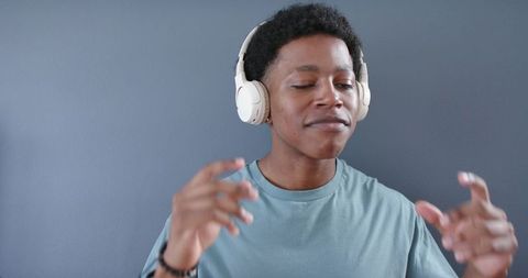 Young man listening to music with white headphones, moving hands, calm minimalist portrait
