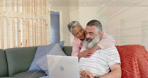 Senior couple embracing while using laptop on cozy sofa, showing digital togetherness
