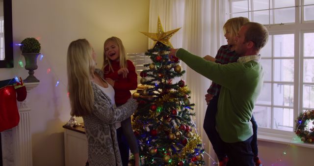 Caucasian family enjoys holiday festivities at home. They're sharing a joyful moment decorating the Christmas tree together.