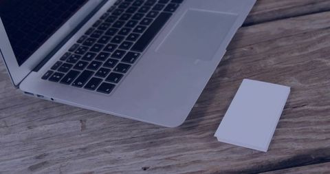 Silver laptop keyboard and blank business cards on weathered wood desk, minimalist workspace