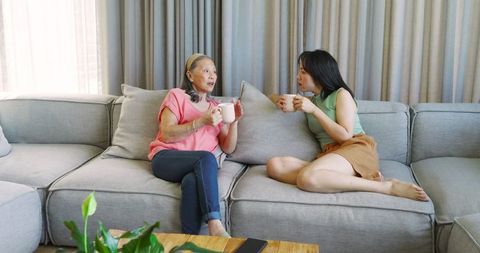 Mother and daughter conversing on modern sofa with mug