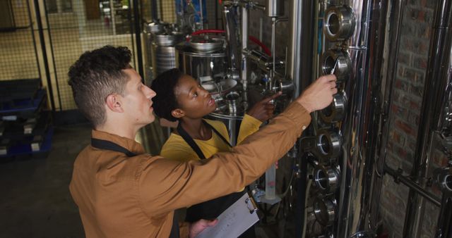 Diverse male and female colleague at gin distillery inspecting equipment and discussing. work at an independent craft gin distillery business.