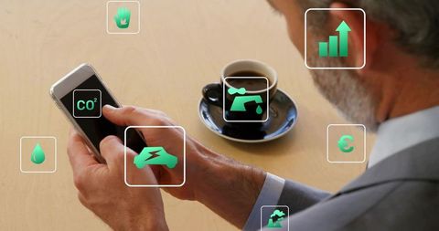 Senior executive tapping smartphone showing sustainability dashboard with ar icons and coffee