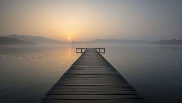 Serene sunrise over foggy lake with wooden dock
