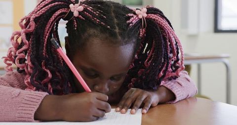 Focused young girl writing in classroom with pink pencil
