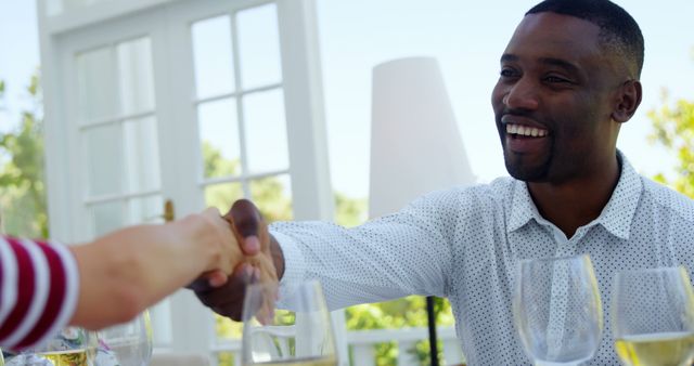 African American man in a casual setting shares a friendly fist bump with another person, with copy space. Their smiling exchange suggests a moment of celebration or agreement during a social gathering.