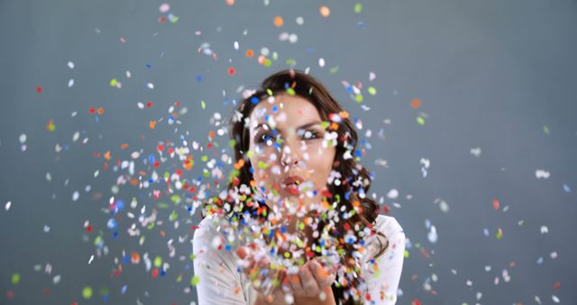 Woman blowing colorful confetti on gray background. Perfect for use in holiday or celebration-themed promotions, party invitations, and festive event advertisements.
