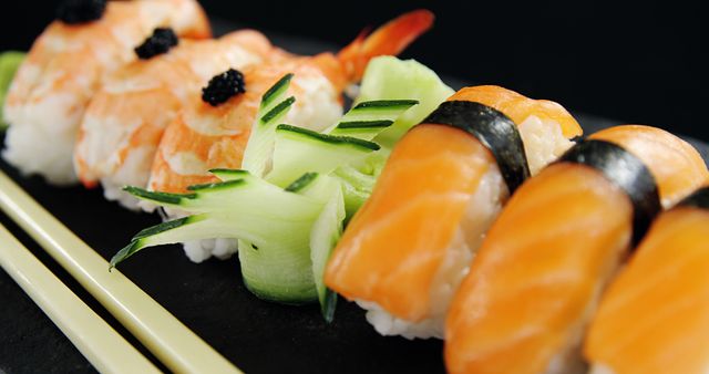 A selection of sushi, including nigiri topped with salmon and shrimp, is elegantly presented on a dark surface, complemented by a pair of chopsticks. Sushi is a traditional Japanese dish that has gained international popularity for its delicate flavors and artistic presentation.