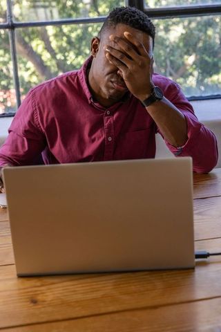 Worried Man Covering Face While Using Laptop in Office