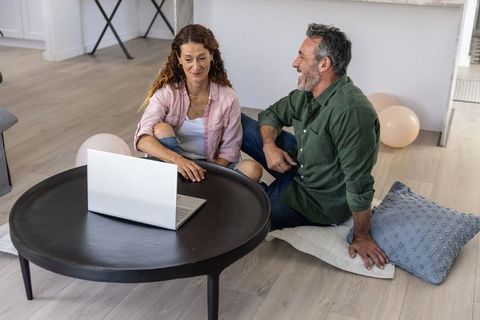 Middle-aged couple sitting on floor sharing laptop in cozy living room planning together