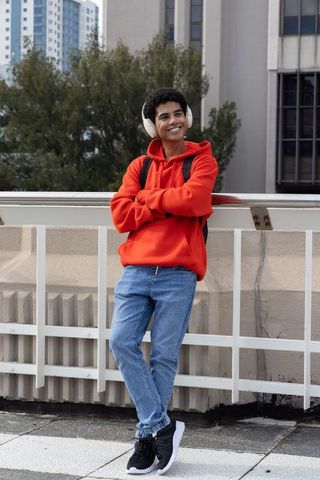African american teen leaning on rooftop railing in red hoodie with headphones