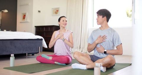 Couple practicing seated breathing on yoga mats in sunlit bedroom for mindfulness