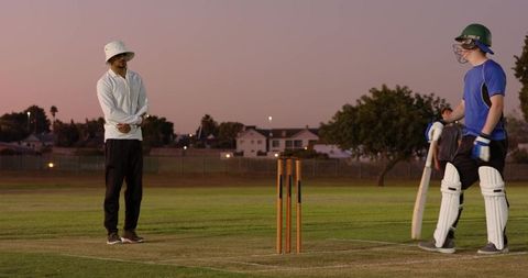Dusk cricket practice with diverse teammates, batsman at crease, wicket and coach guidance