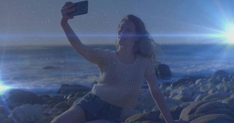 Woman Taking Selfie on Rock by Ocean at Dusk