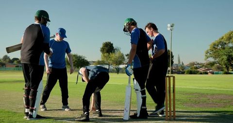 Young cricket team inspecting pitch before match on sunny community ground with stumps