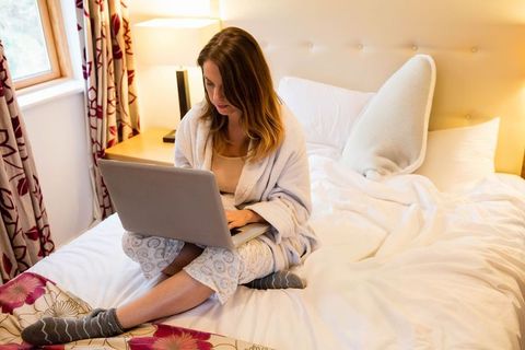 Woman Relaxing in Minimalist Bedroom Using Laptop