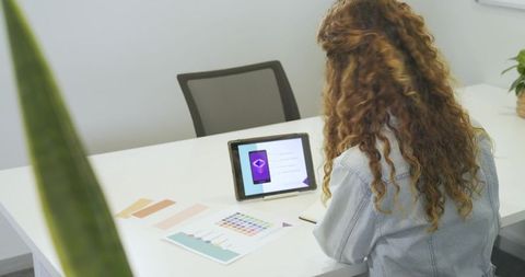 Mature woman reviewing tablet and color swatches at minimalist sunlit office desk