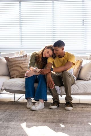 Young diverse couple sitting on sofa leaning together with smartwatch showing intimacy