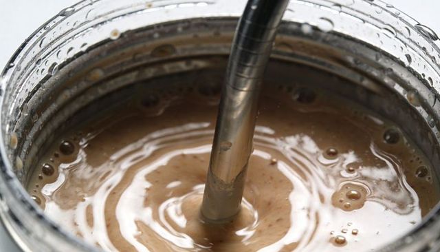 Blending creamy nut butter in clear jar with immersion blender, close-up