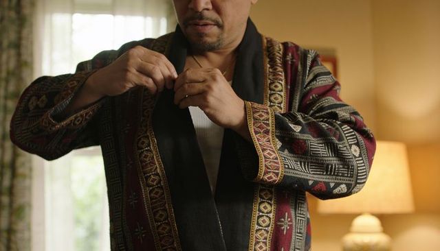 Middle-aged man fastening ornate embroidered robe in cozy bedroom morning scene
