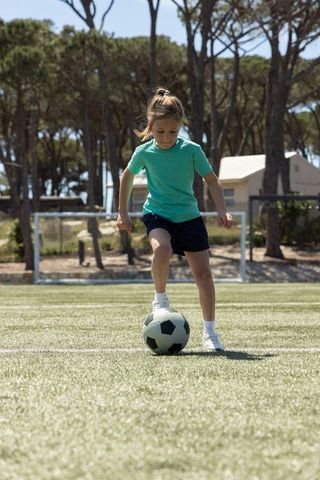 Young girl dribbling soccer ball on artificial turf showing focus and skill