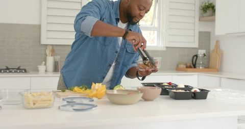 African american man meal prepping at bright modern kitchen island with glass bowls