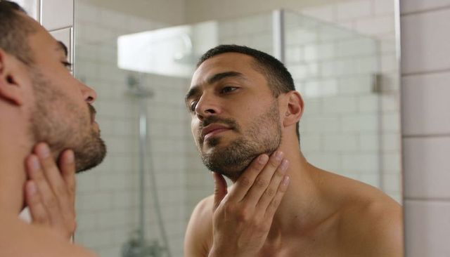 Man checking stubble in mirror while touching jawline and grooming facial hair
