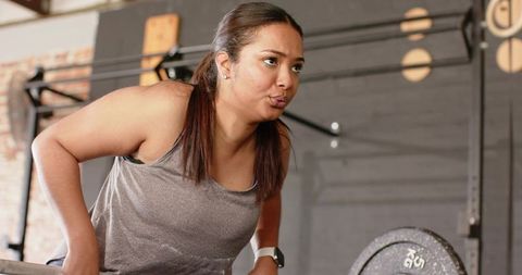Young woman doing dips on bars in industrial gym with weight plate for upper-body strength