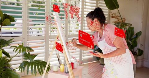 Artist painting on canvas in bright sunroom surrounded by plants with red data overlay