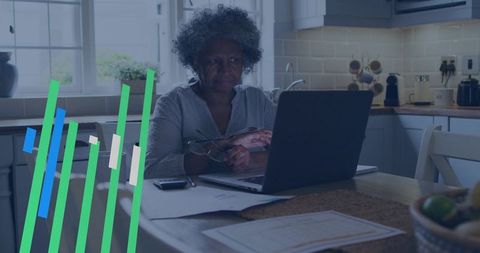 Senior woman reviewing finances from home, working on laptop with reading glasses