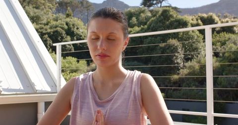 Young woman practicing meditation on sunlit balcony with greenery and serene mountain view
