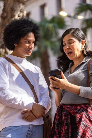 Friends sharing smartphone conversation in sunny urban plaza with palm trees