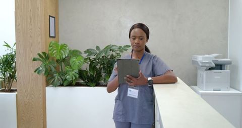 African nurse standing at clinic reception holding tablet, wearing id badge and smartwatch