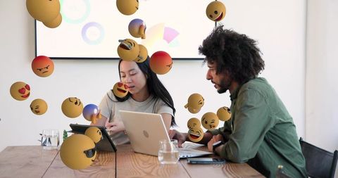 Team collaborating on laptops and tablet with floating emoji reactions in modern office