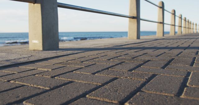 Photo showing an empty paved coastal walkway with railings overlooking a calm ocean. Ideal for illustrating seaside walks, tranquil outdoor settings, nature escape, tourism promotion, relaxation themes, or urban infrastructure near the sea.