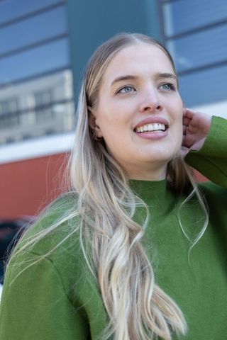 Smiling blonde woman in green sweater looking upward, urban lifestyle portrait in daylight