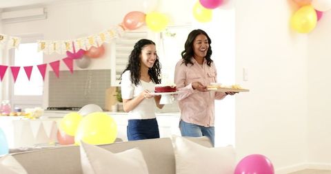 Two women carrying cake and snacks at birthday celebration
