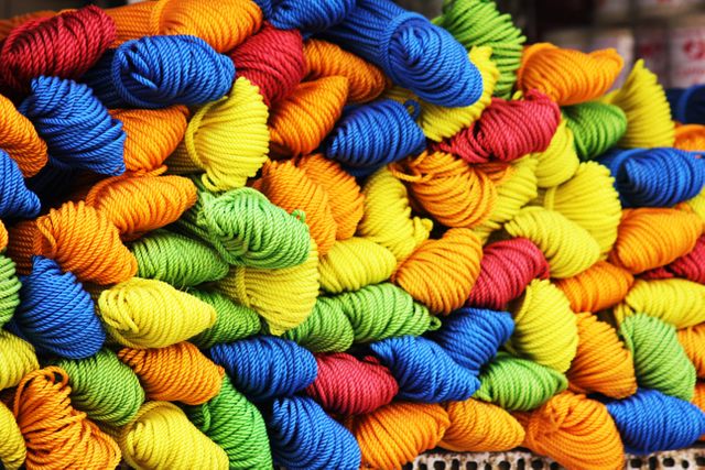 Brightly colored yarn skeins stacked neatly in a pile. This image is ideal for craft and knitting websites, blogs about textile arts, or advertisements for yarn and craft supplies. The vivid colors attract attention and inspire creativity in any crafting-related project.