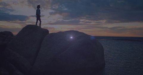 Silhouette of Woman Exploring Rocky Shoreline at Sunset