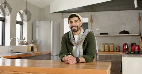 Smiling indian man leaning on wooden kitchen island in modern rustic home