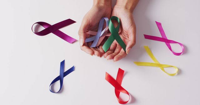 Image of hands of caucasian woman holding colorful ribbons on white background. medicine, health, cancer awareness concept digitally generated image.
