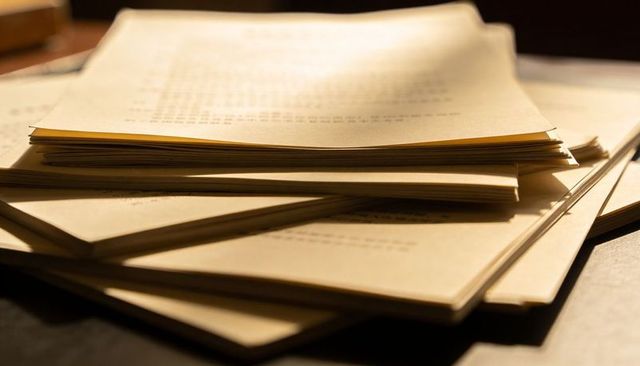 Stack of Vintage Printed Sheets on Wooden Desk Casting Warm Shadows and Cozy Light