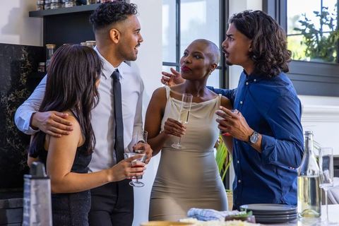 African american woman with friends clinking glasses, chatting in sunlit modern kitchen