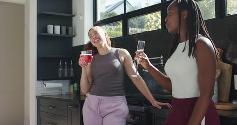 Friends chatting and laughing with drinks in sunlit modern kitchen