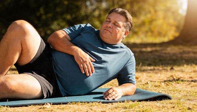 Middle-aged man practicing relaxation on yoga mat in sunlit park