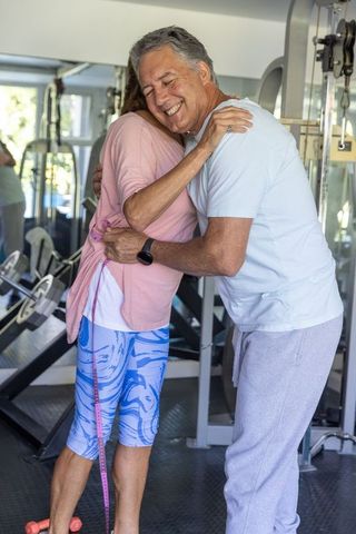 Active senior couple hugging in gym celebrating fitness progress and healthy lifestyle