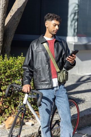 Asian man checking smartphone while standing with bicycle on sunny urban sidewalk