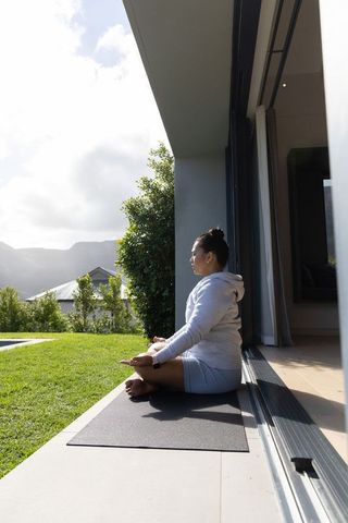 Woman meditating on patio threshold facing green lawn and distant mountain ridge morning calm