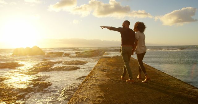 Couple walking together along a path with the ocean and sunset in the background. Perfect for advertisements about travel, romance, relationships, and tourism. Suitable for illustrating articles about romantic getaways, outdoor activities, serene moments, and beach vacations.